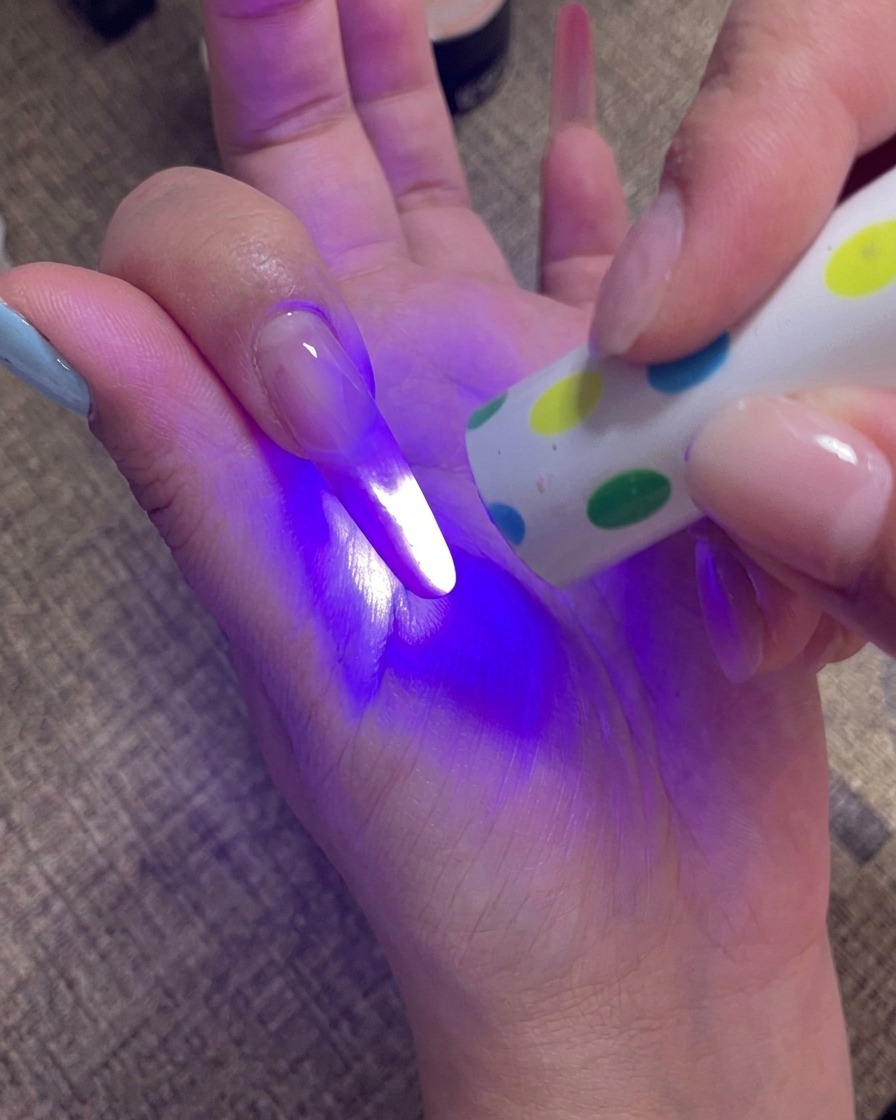 A hand holding a portable UV lamp directly over the fingernails to cure the final gel layer.