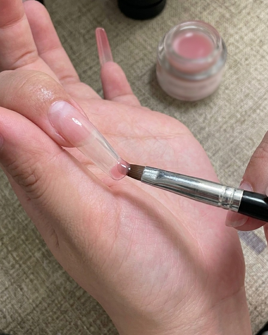 A nail art brush applying and blending gel at the tip of the nail.