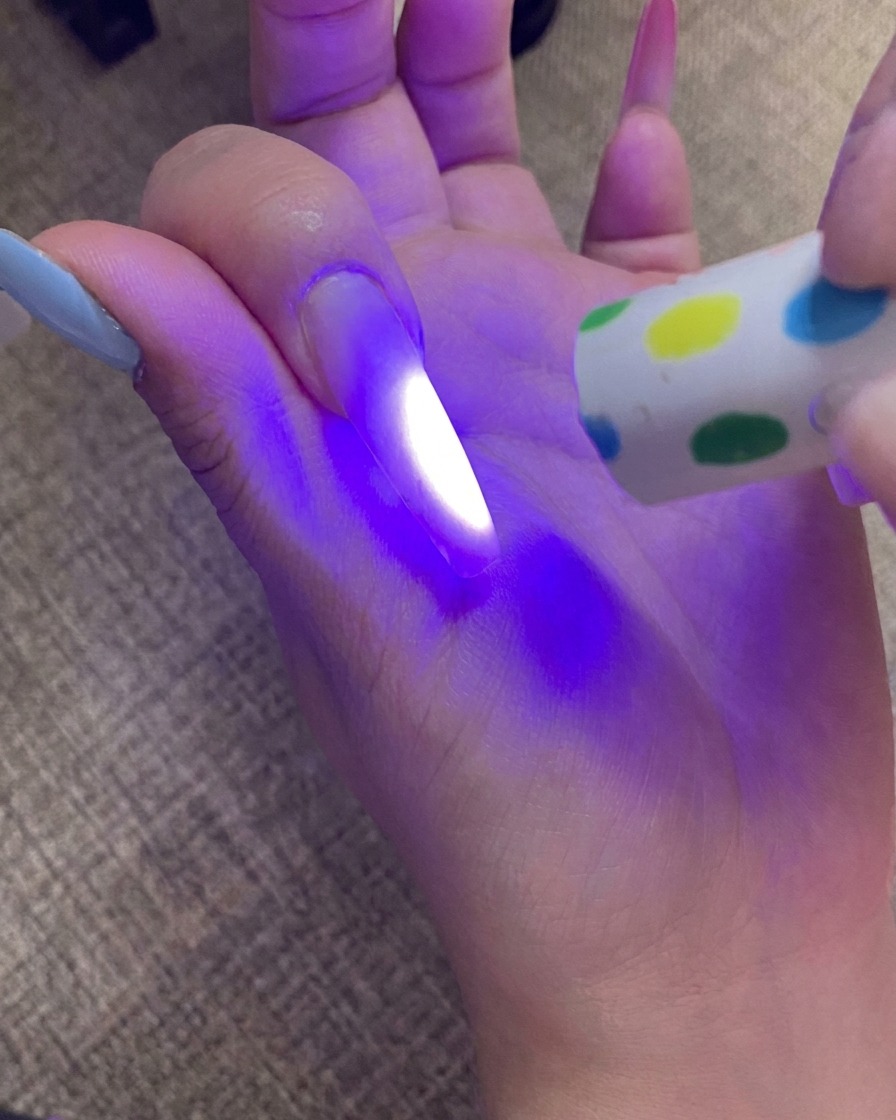 A hand curing the ombre-tipped nail under a UV lamp, with the light illuminating the nail.
