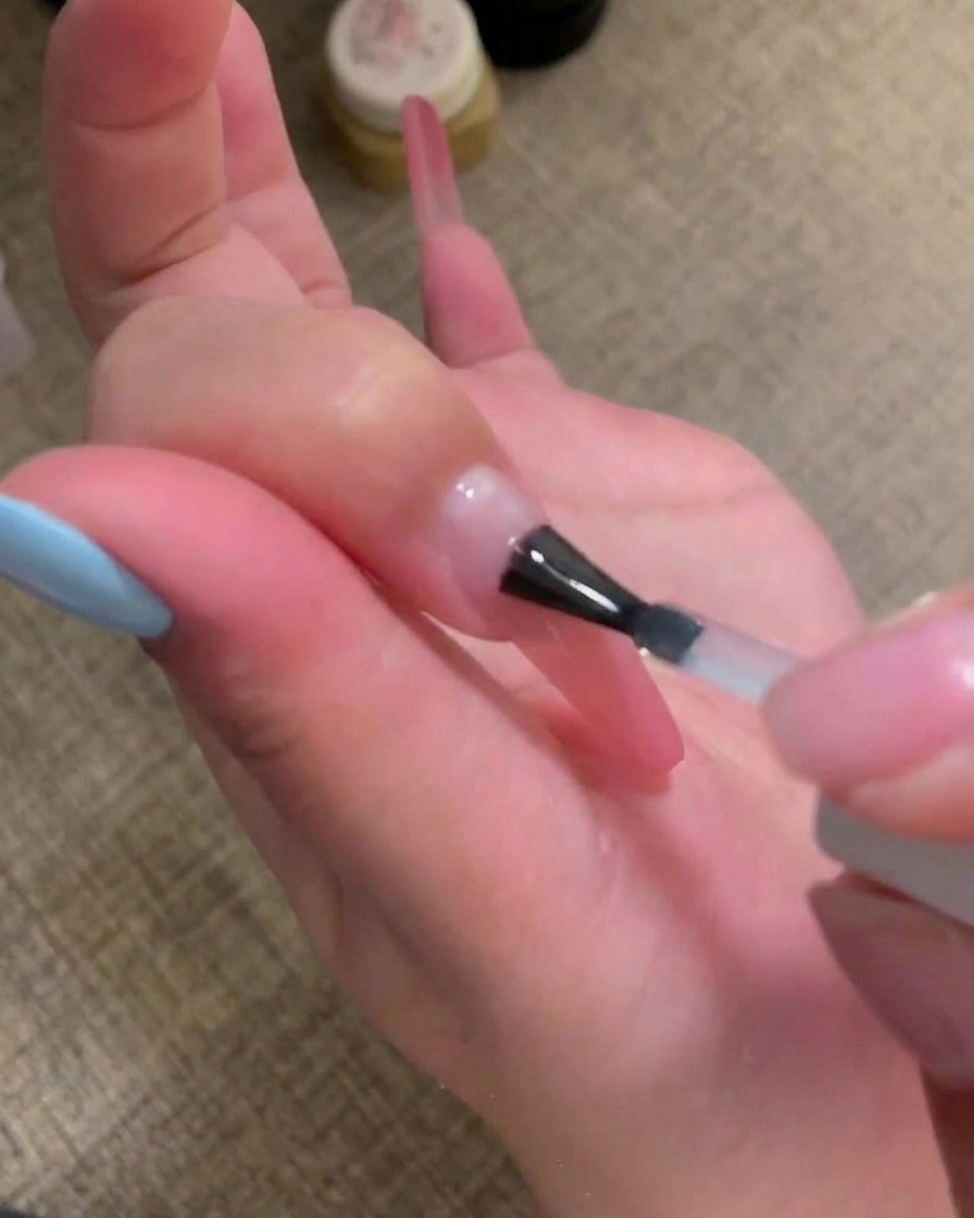 A brush applying a clear, glossy base coat onto the nail surface.