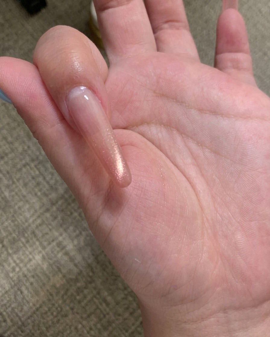 A close-up of a magnetic nail tool being held over a nail coated in champagne-colored cat eye gel, showing the particles shifting into a line.