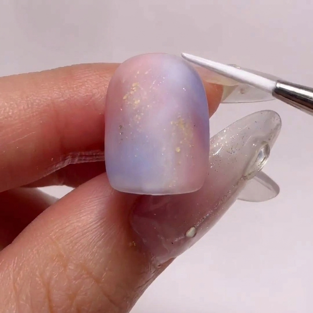 A fine-liner brush creating delicate white ripple patterns on a matte-finished, gradient nail.