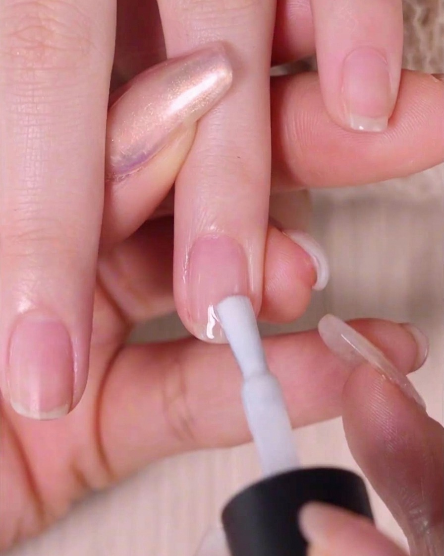 A close-up of a hand using a nail polish brush to apply a thin, even layer of sheer white polish onto a natural fingernail.
