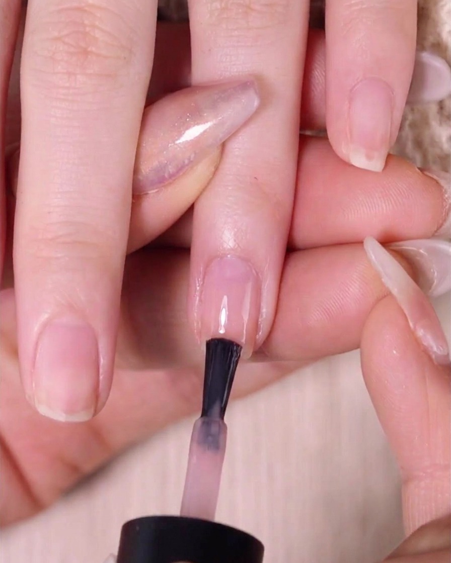 A brush applying a second coat of nude pink polish to the top half of the fingernail over a previously blended layer.