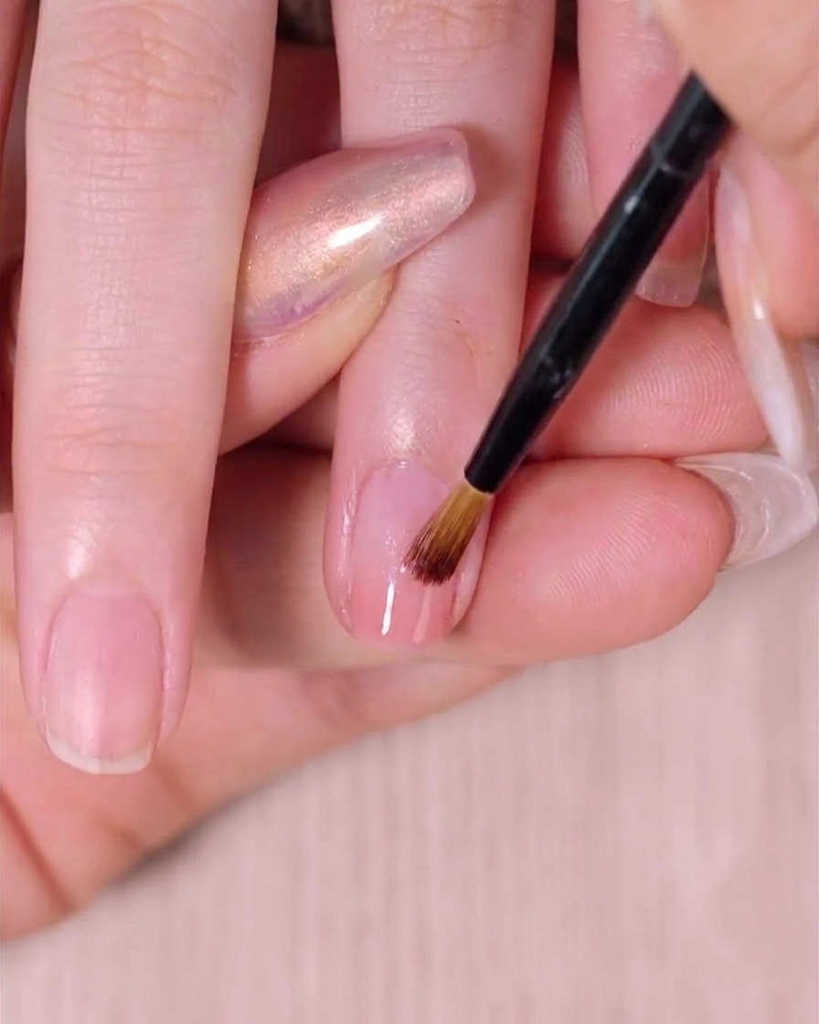 An ombre nail brush gently sweeping the second layer of pink polish to perfect the gradient fade on a fingernail.