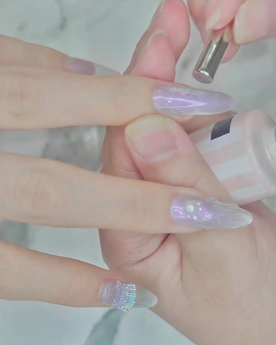 A cylindrical magnet tool positioned over a nail with wet silver polish to create a cat-eye effect.