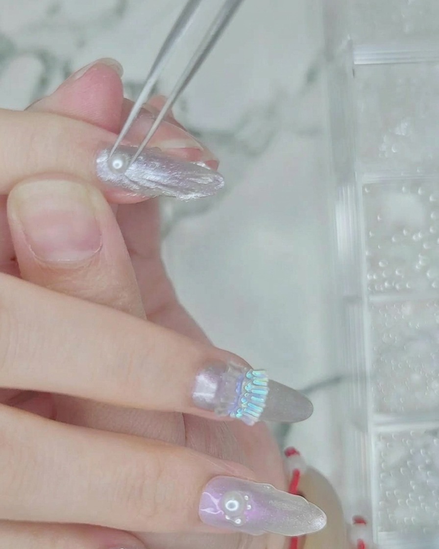 Tweezers placing small white pearl beads into a line of wet clear gel on the nail.
