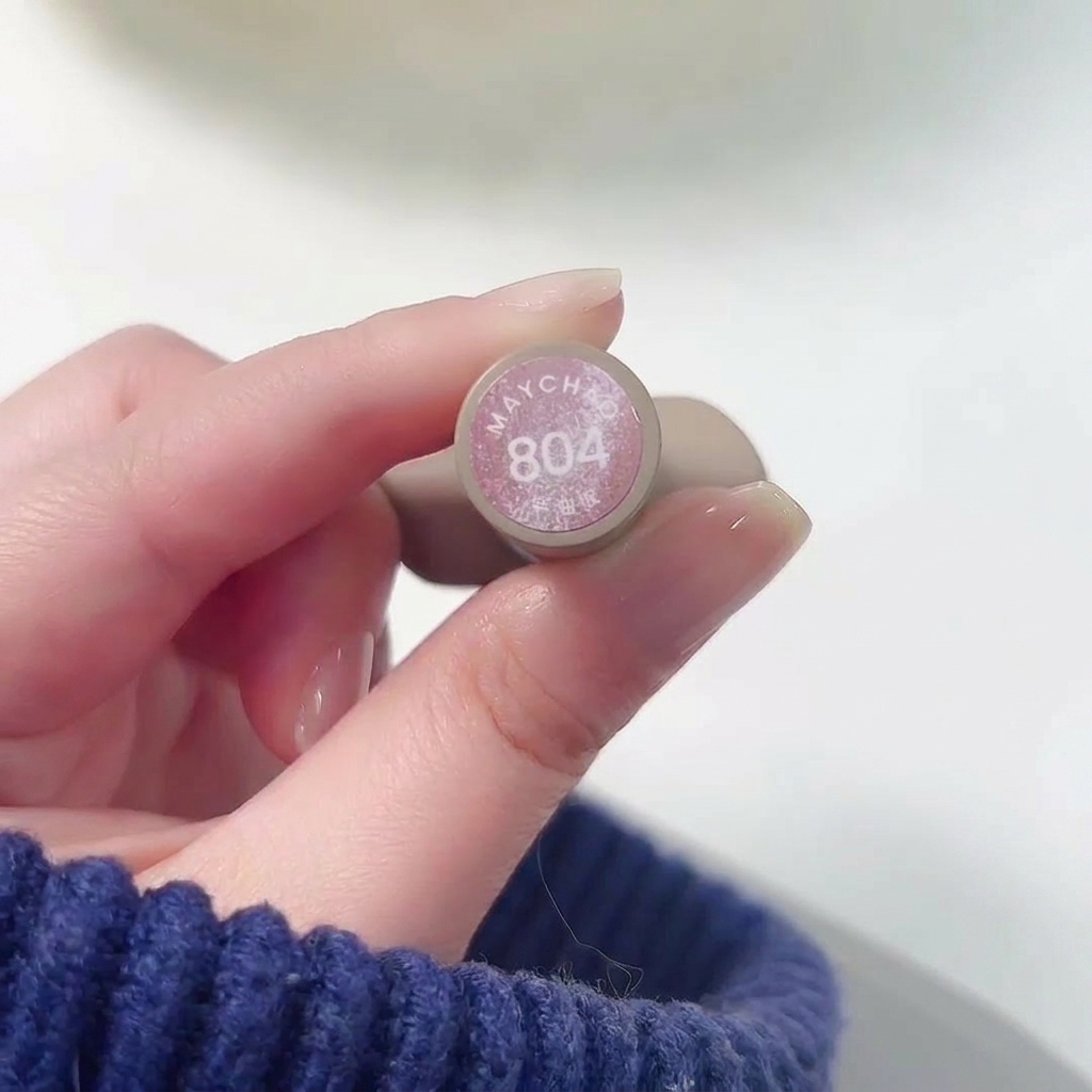 A close-up of a hand holding the bottle of Meichao 804 Taozhi Yaoyao while applying the shimmering nude pink polish to a fingernail.
