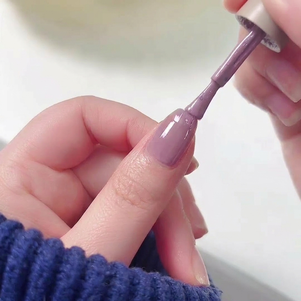 A nail polish brush applying purple gel polish to the top half of a fingernail over a pink base.