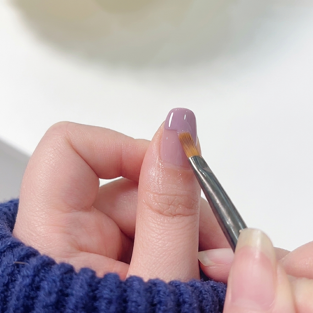 A flat nail art brush gently sweeping the lower edge of purple tip polish downwards into a pink base to create a seamless gradient.