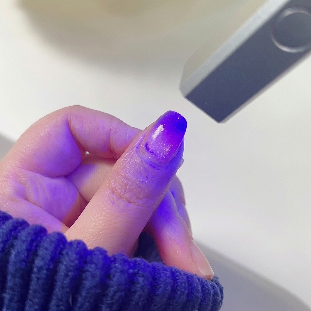 A thumb nail with a blended pink and purple gradient curing under the purple light of a mini LED nail lamp.