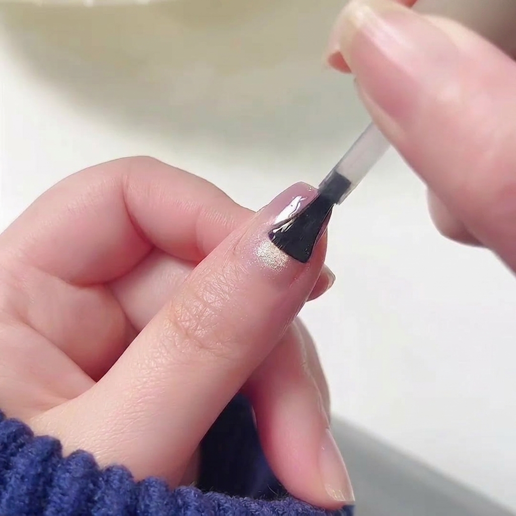 A brush applying a clear, high-gloss top coat to the surface of a nail that already features a seamless pink and purple gradient design.