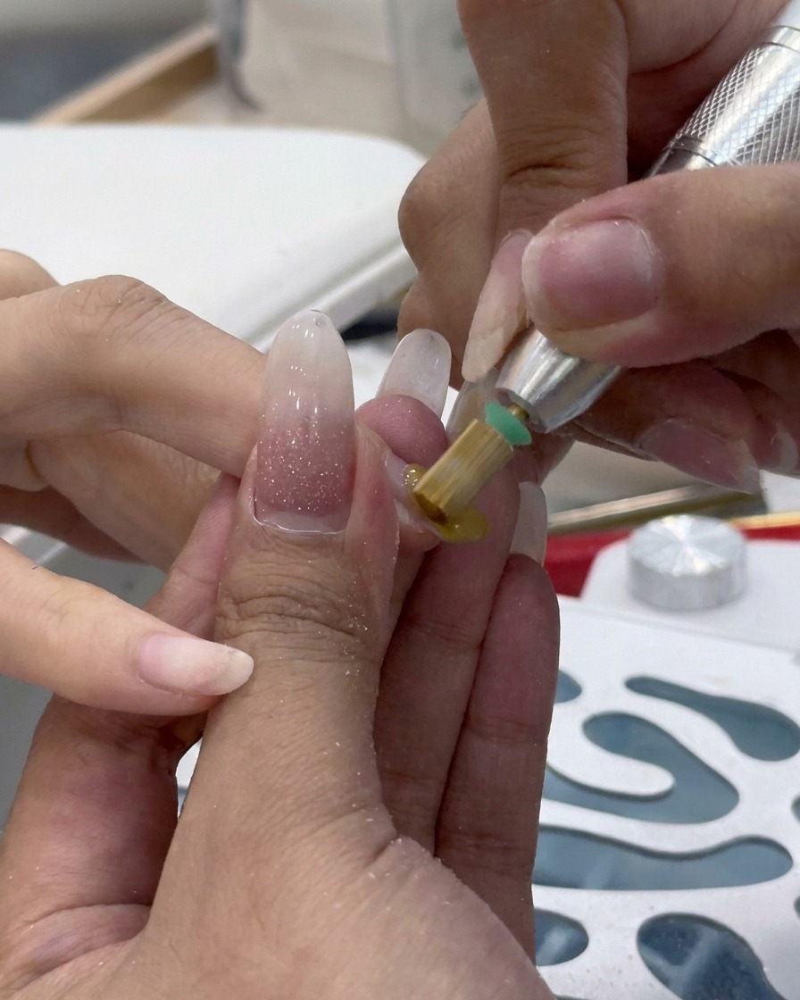 Close-up of an electric nail drill with a sanding band removing old product from a nail.