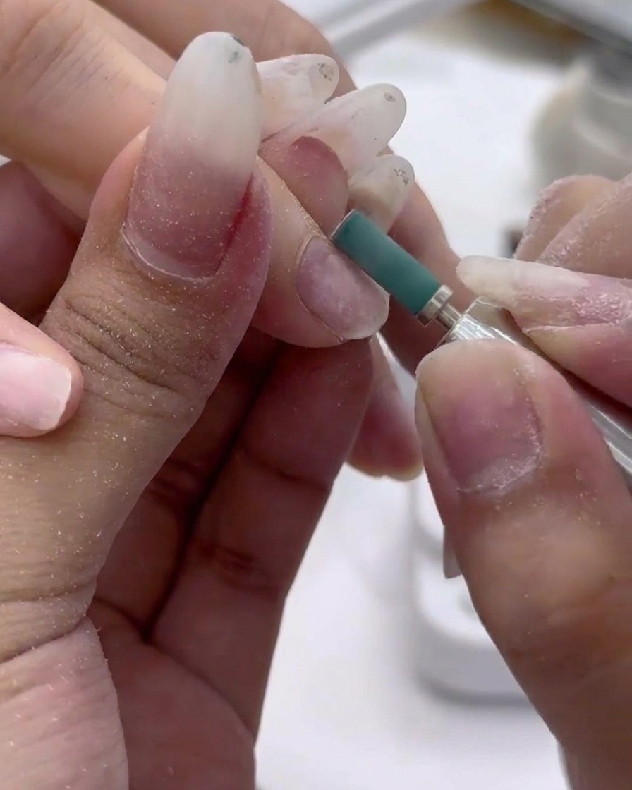 Close-up of a green sanding band gently buffing the surface of a natural nail.