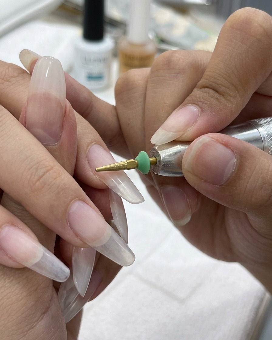 A gold cone-shaped drill bit smoothing the transition line between a clear nail tip and the natural nail bed.