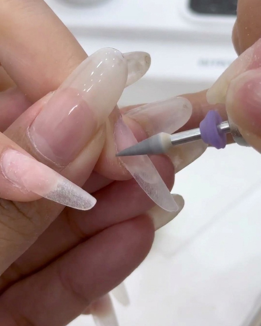 A grey tapered drill bit refining the sidewalls and cuticle area of a prepped nail.
