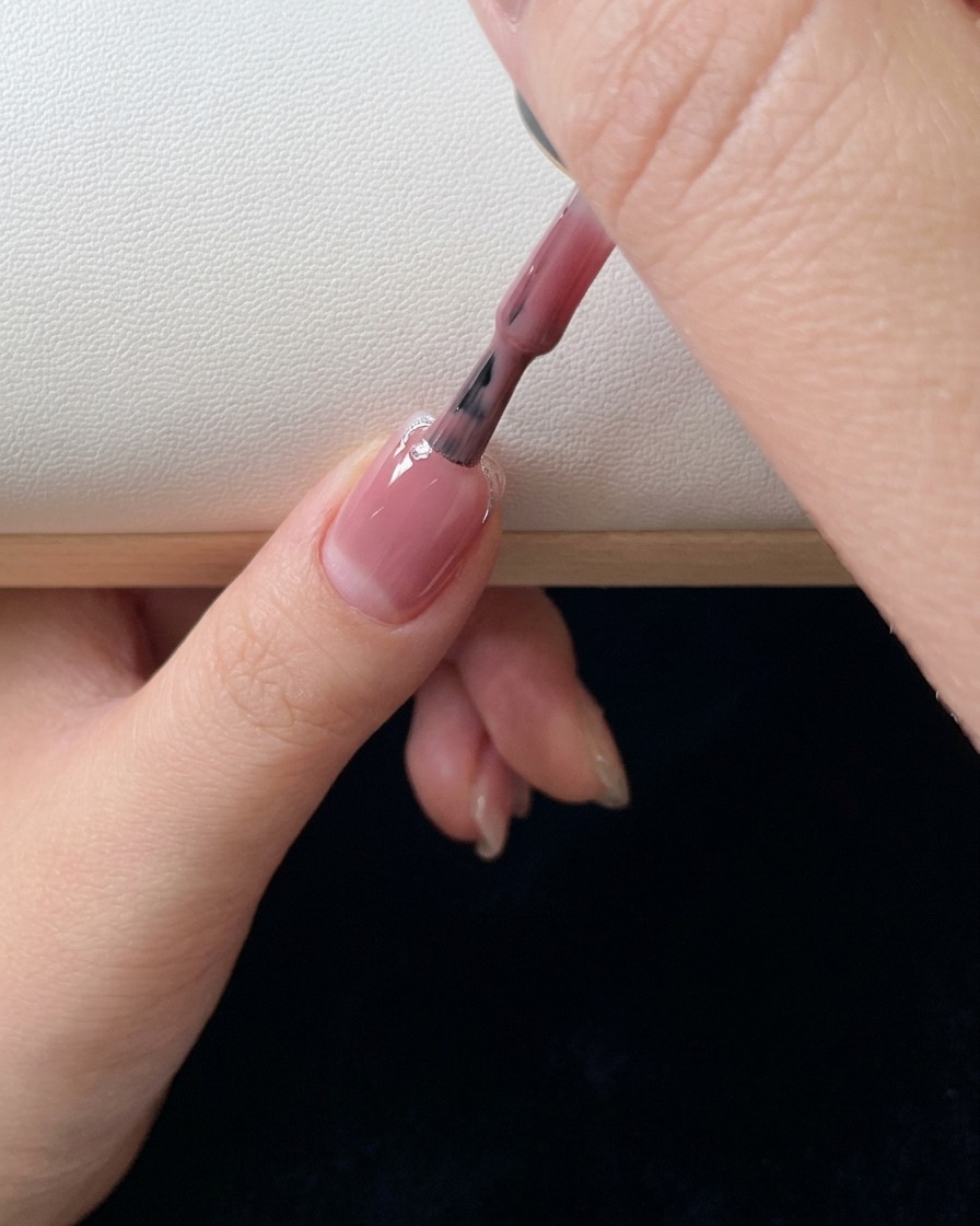 A close-up of a brush applying a second coat of pink gel polish and blending the color down the nail.