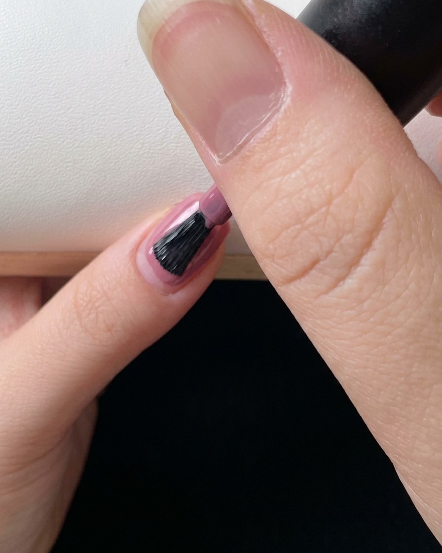 A close-up of a nail brush applying a final layer of pink gel polish to perfect the gradient effect.
