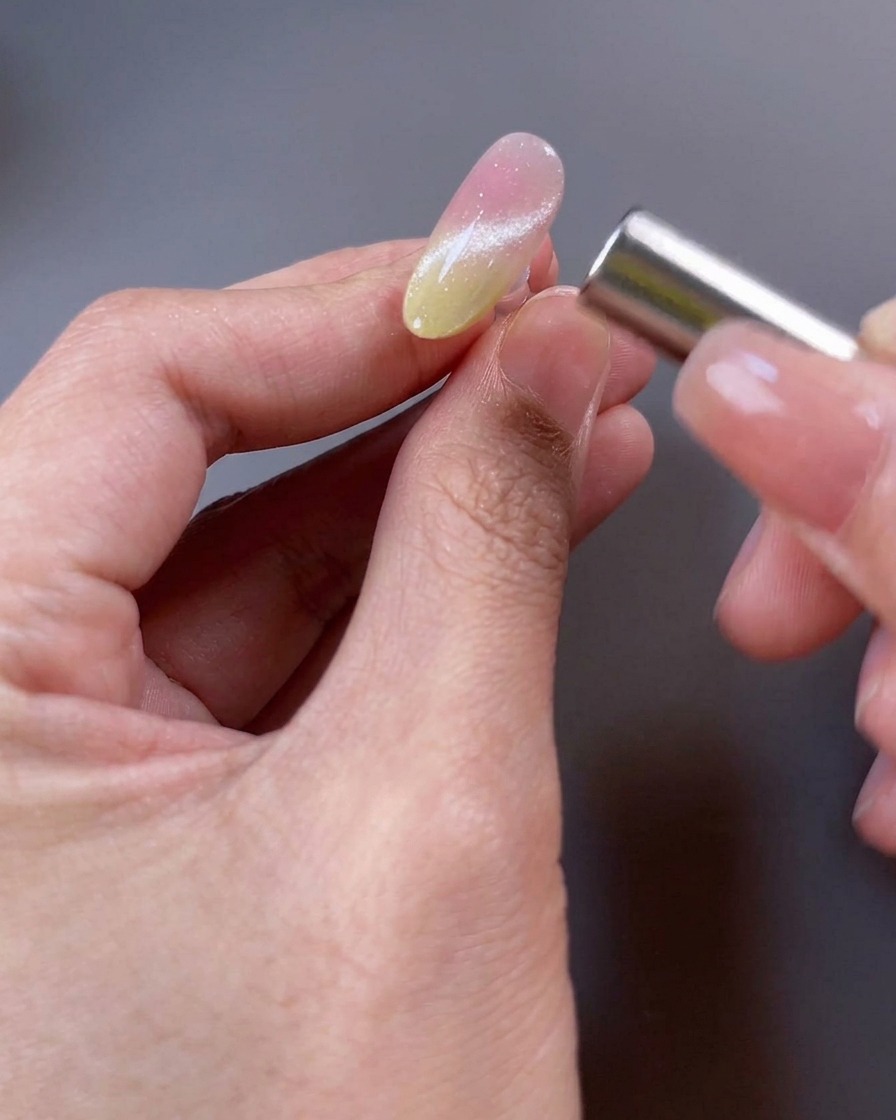 A close-up of a nail with magnetic gel polish, with a magnet held near the surface to manipulate the shimmer particles into a wide beam.