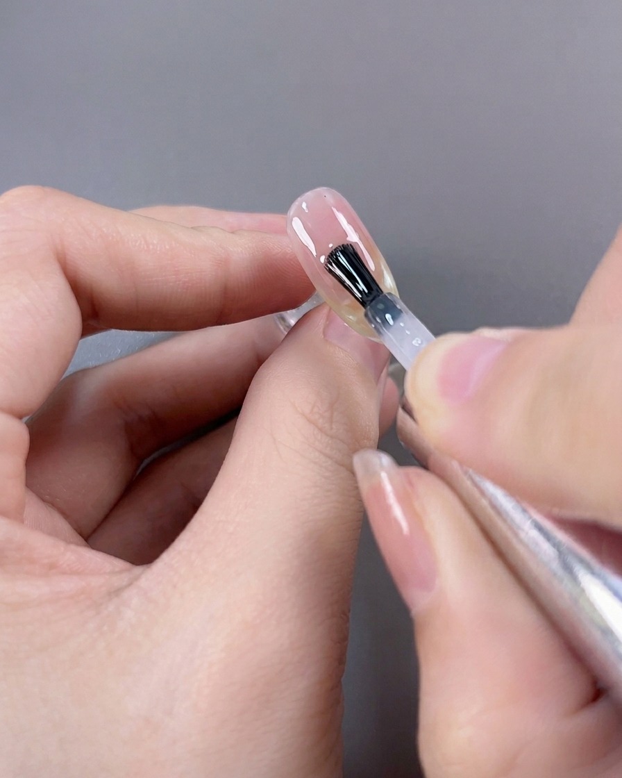 A brush applying a final, high-gloss top coat over a finished cat-eye French manicure.