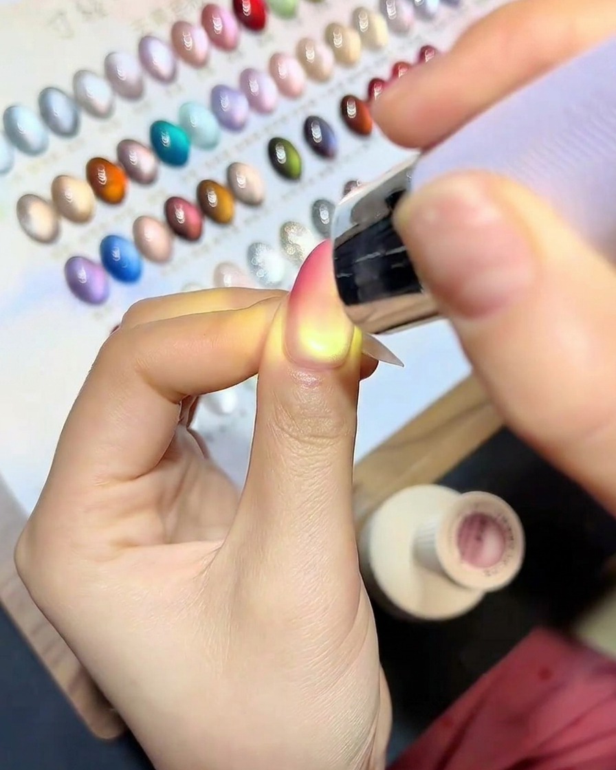 A brush applying a clear, glossy top coat over the finished cat-eye gradient nail.