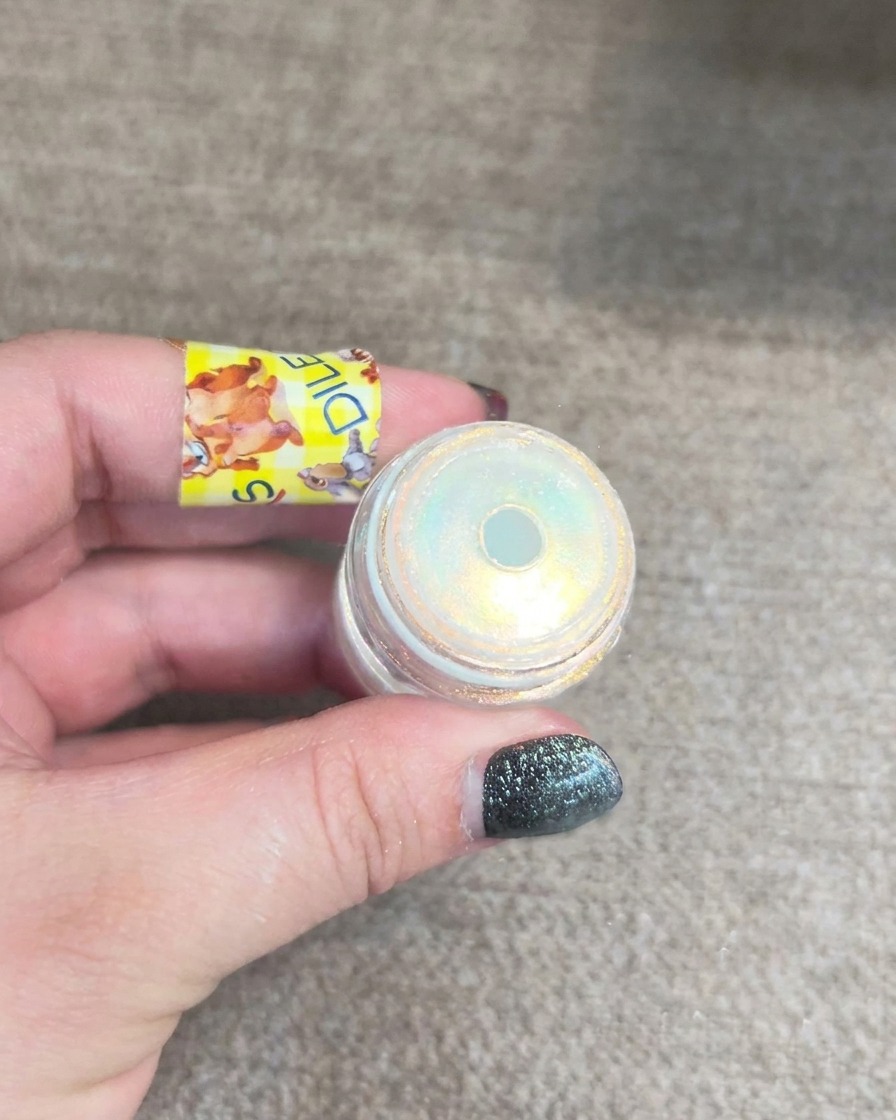 A small jar of aurora nail powder showing a multi-dimensional yellow and blue shimmer.