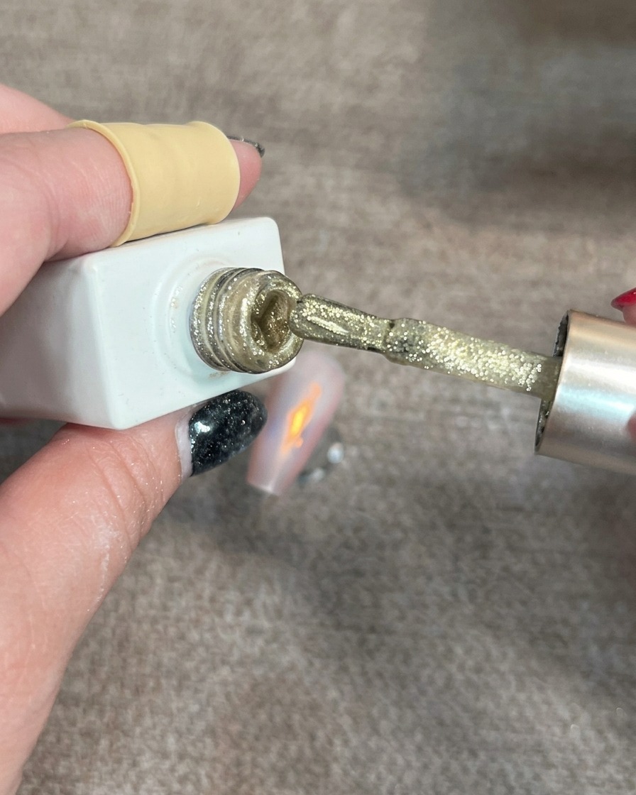 A nail brush applying small, shimmering gold cat-eye gel spots onto a partially decorated nail.