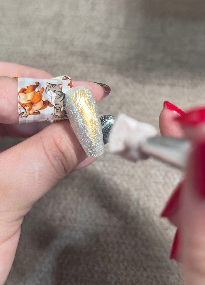 A blending brush dabbing orange blush gel onto a shimmering, multi-toned nail to create a soft gradient.