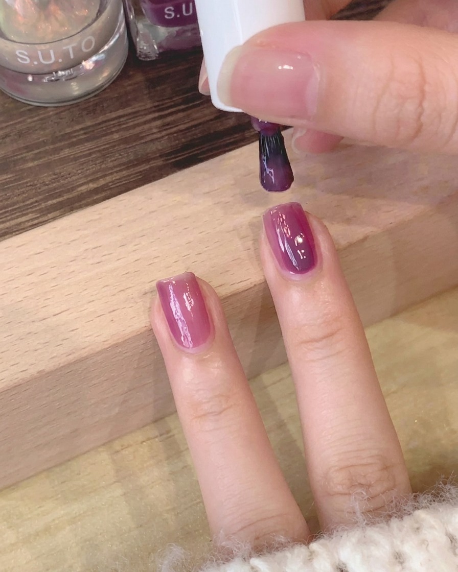 A close-up shot of a brush smoothing the purple gel surface on the nail.