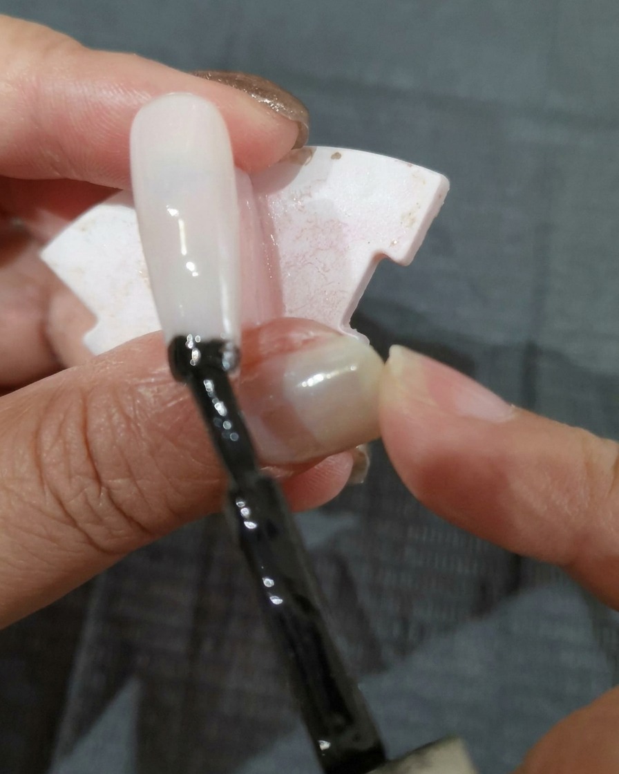 A brush applying a coat of black gel polish onto a nail tip.