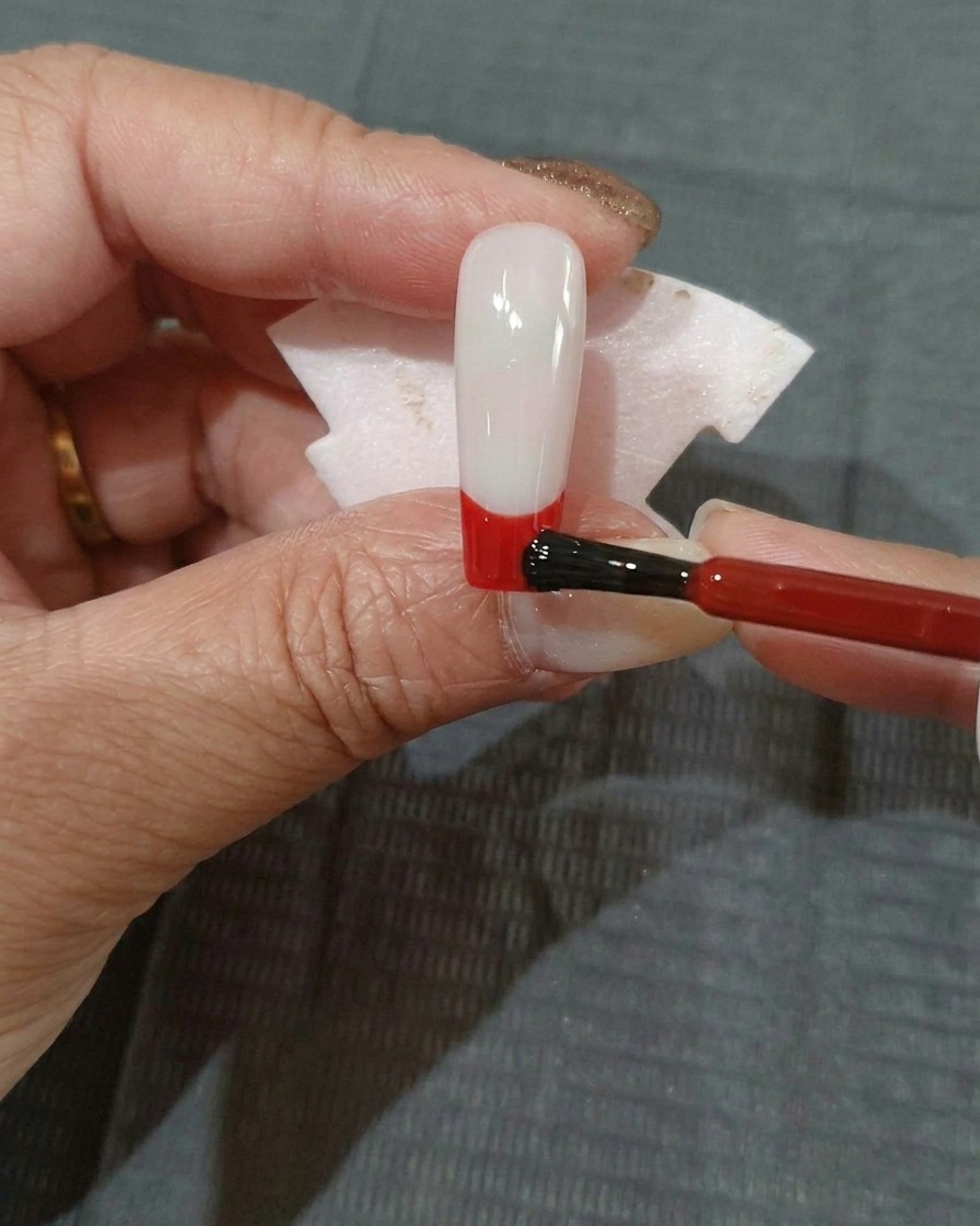 A thin layer of red gel polish being applied over the bottom section of a black-coated nail.
