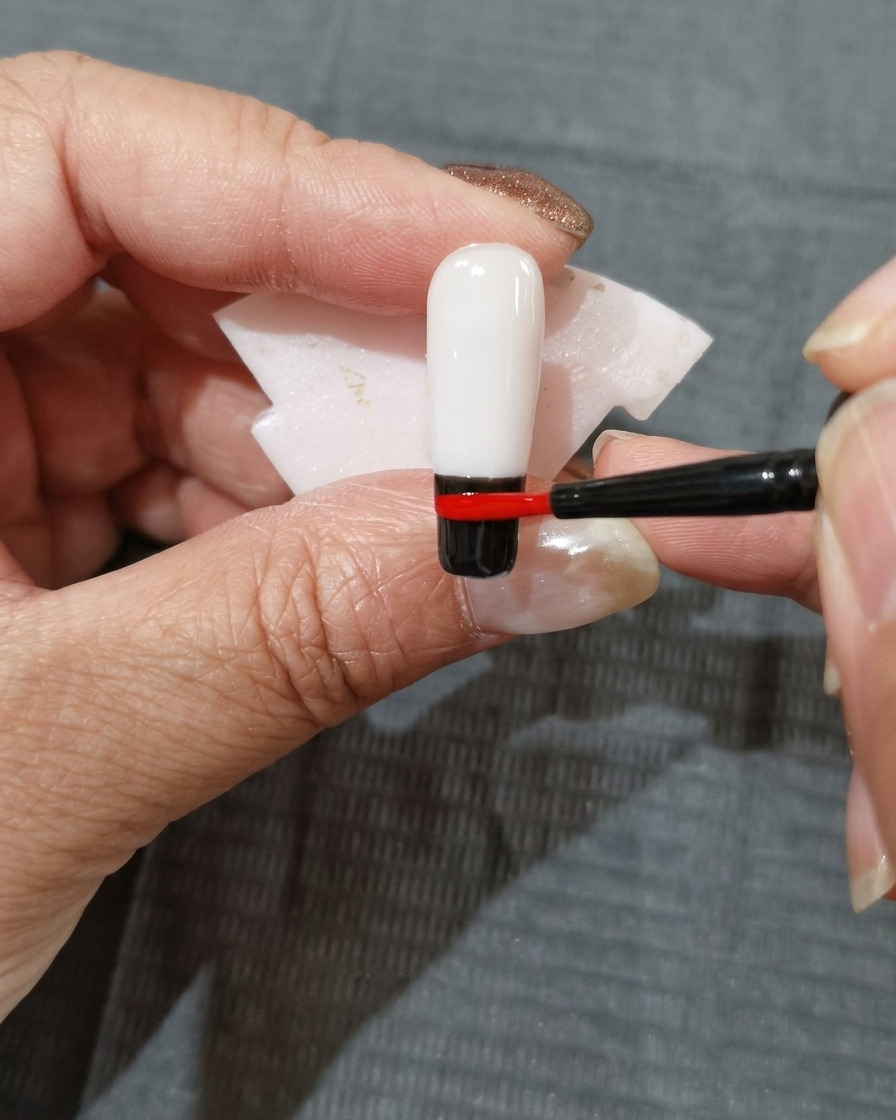 A streak of orange-red gel polish being placed directly above the red color band on the nail.