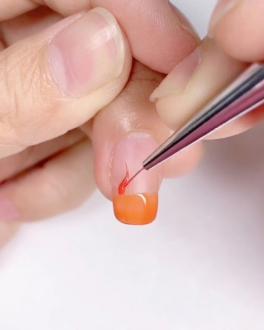A fine liner brush creating flame-like shapes on the orange-tipped nail.