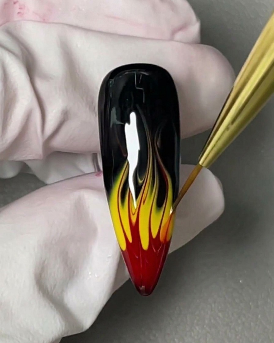 A small brush applying a clear, viscous blooming gel over a glossy black nail.