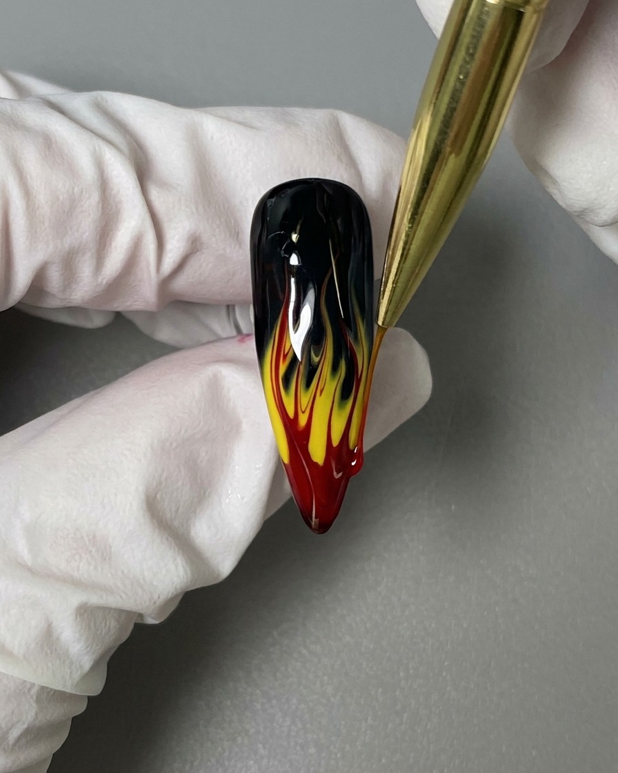 A liner brush applying a glossy top coat over the finished flame nail art design.