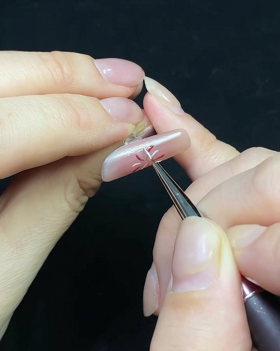 A fine brush applying top coat to a nail with a firework design and a small pearl embellishment.
