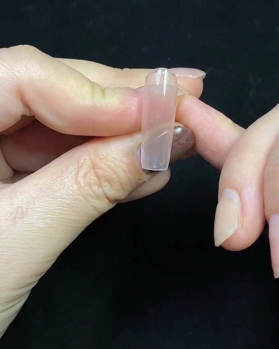 A close-up of a deep red gel French tip being painted on a clear nail extension.