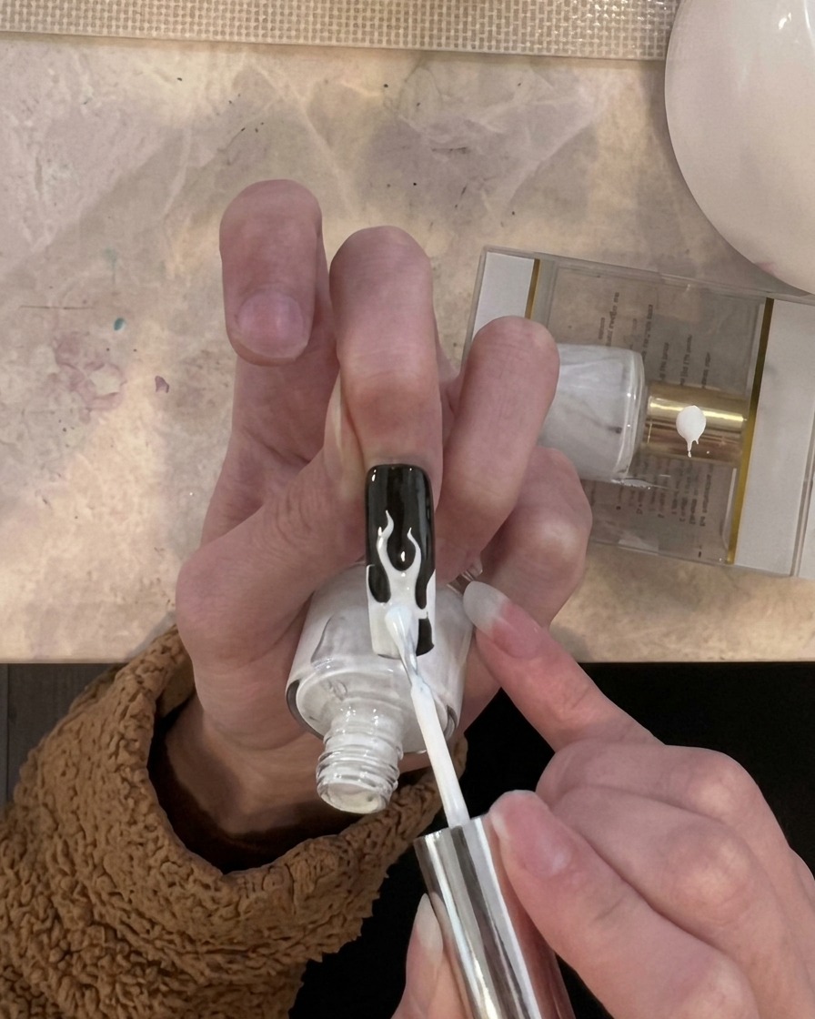 A brush applying a layer of white gel polish specifically to the flame design areas on the nail tip.