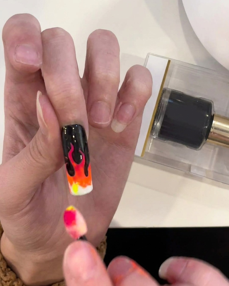 A sponge applicator applying yellow pigment to the final section of the flame gradient at the nail tip.