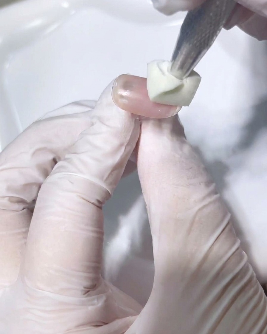 A metal magnetic tool positioned close to a freshly painted nail tip, pulling the shimmering particles toward the free edge.