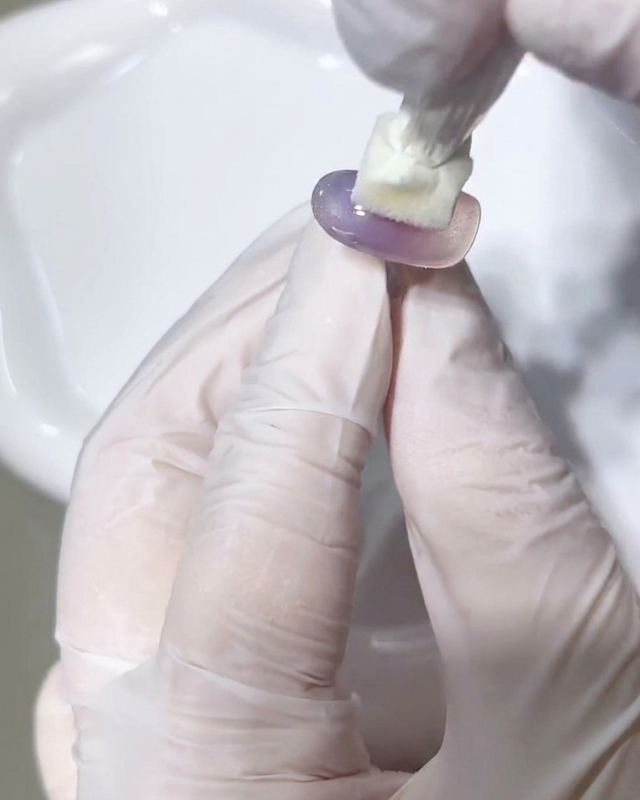 A lint-free wipe being used to clean the surface of a cured gel nail tip.