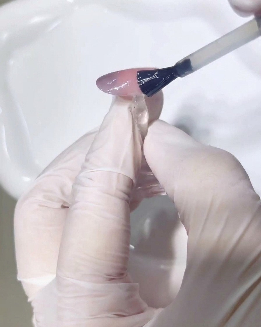 A close-up view of a brush applying a clear, glossy top coat over the finished nail art.