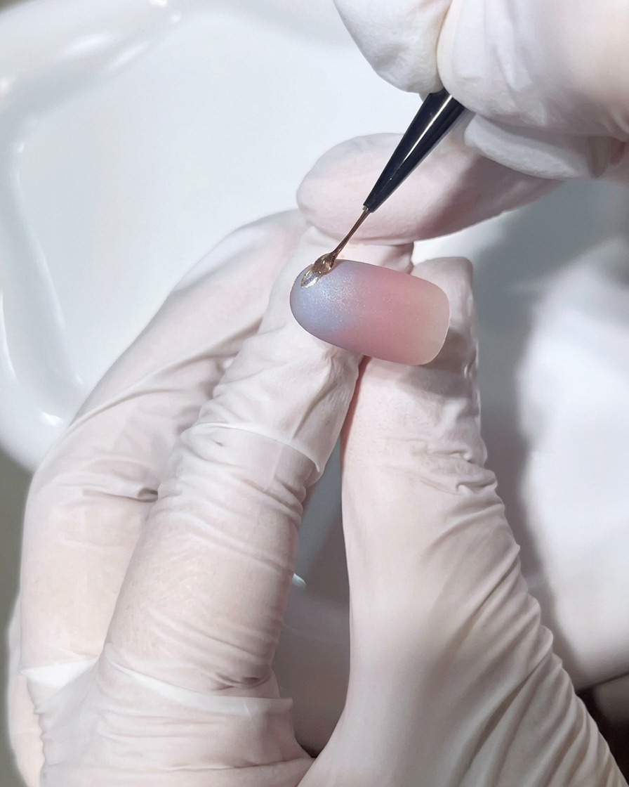 A close-up view showing a detail brush applying a precise bead of clear hard gel onto the nail to form a 3D accent.