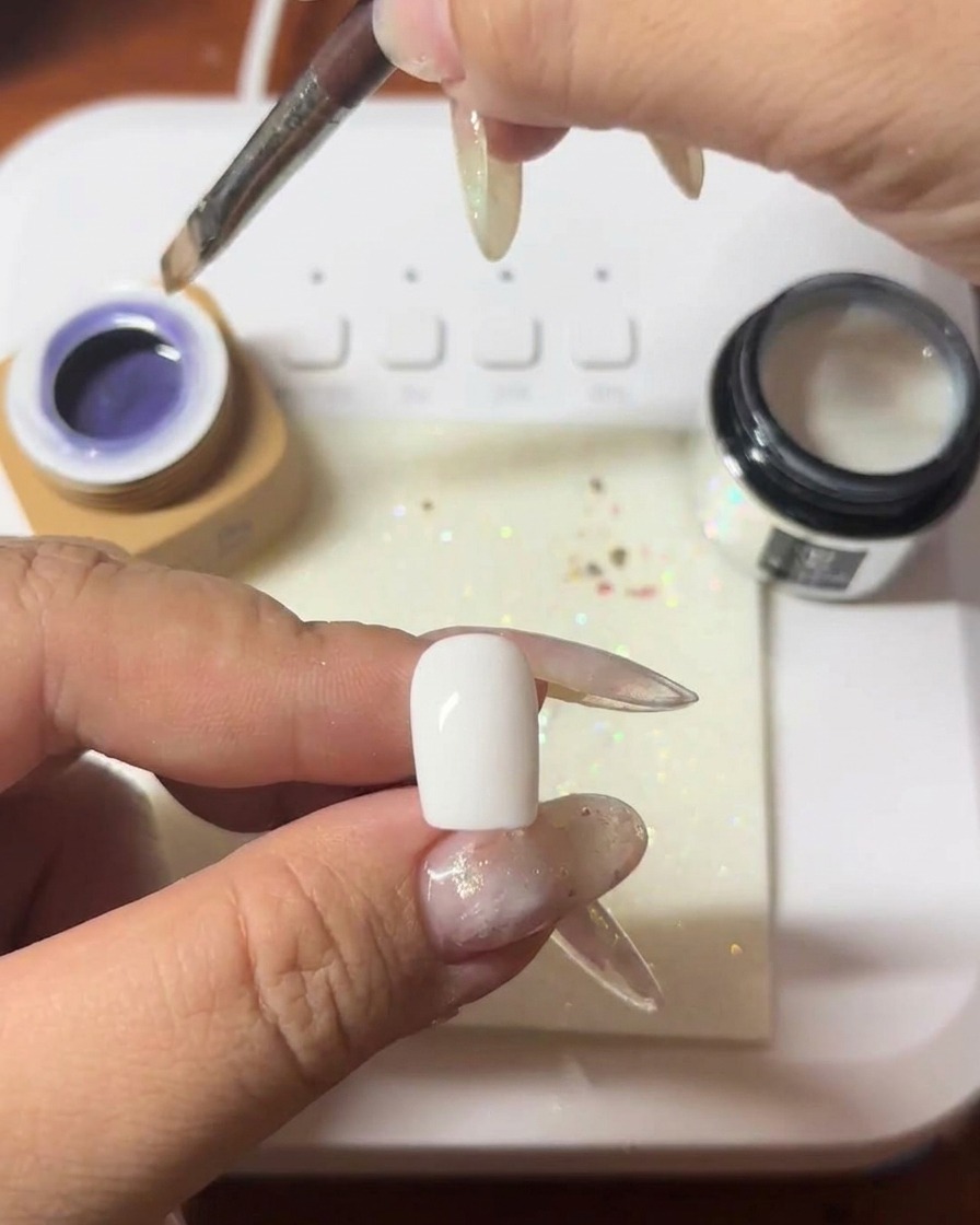 A brush applying a coat of deep purple cat-eye gel to a nail.