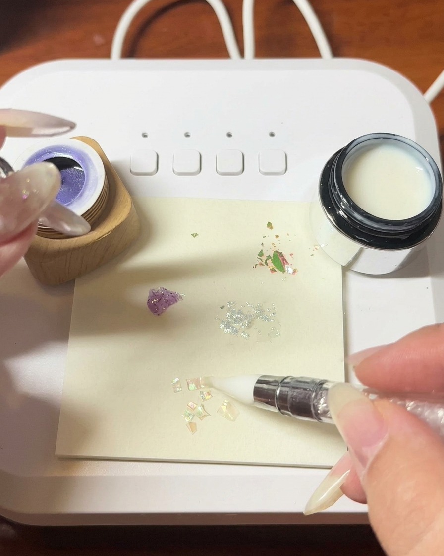 Tweezers placing delicate, iridescent shell fragments onto a wet gel surface.