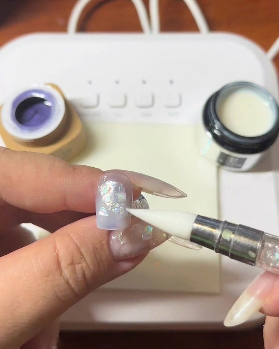 A silicone-tipped tool pressing down on shell pieces on a nail surface.