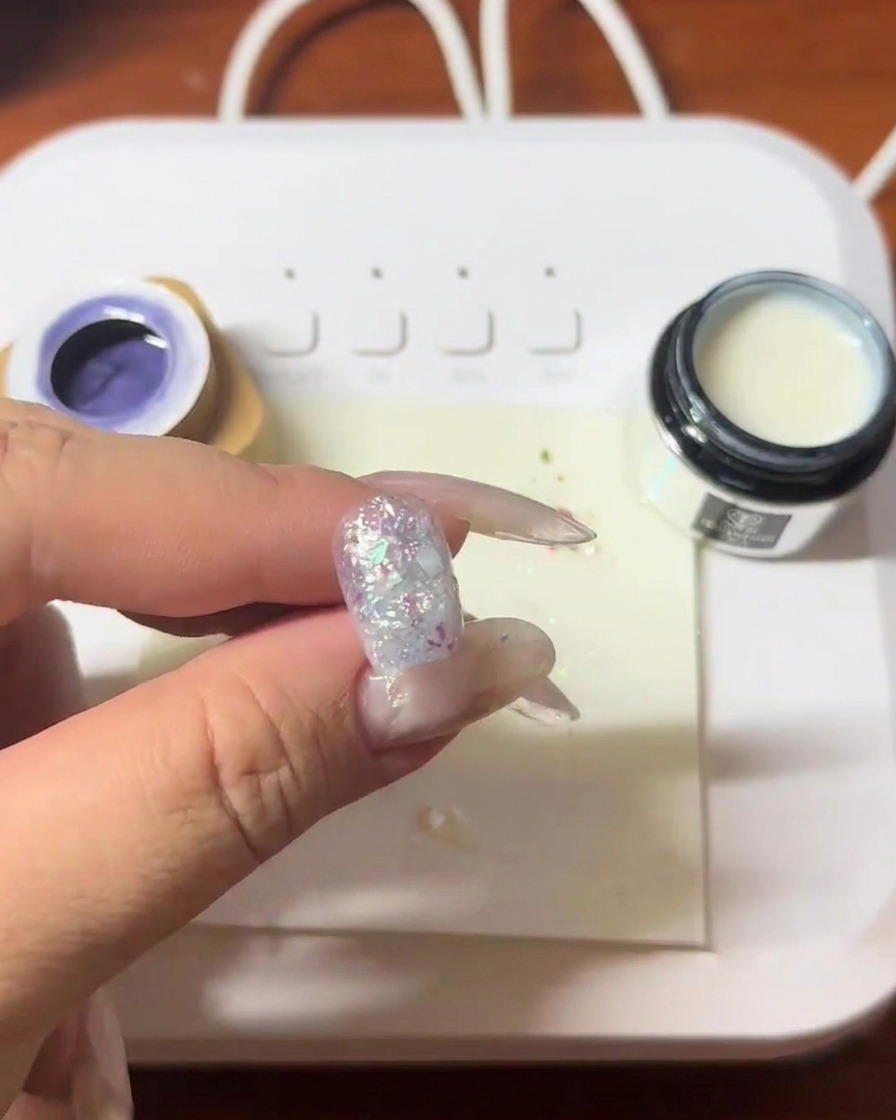 A nail with embedded shell fragments being cured under an LED lamp.