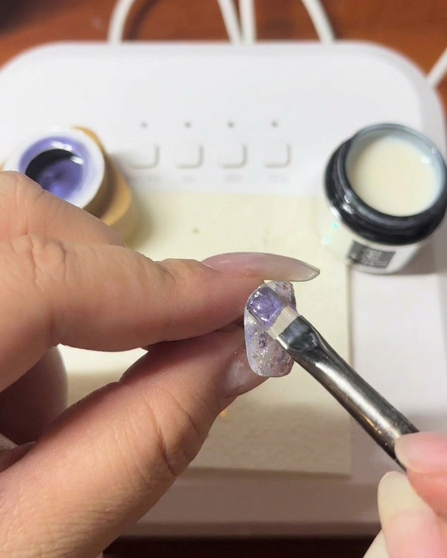 A magnetic tool being held near a nail to create a shimmery cat-eye line in the purple gel.