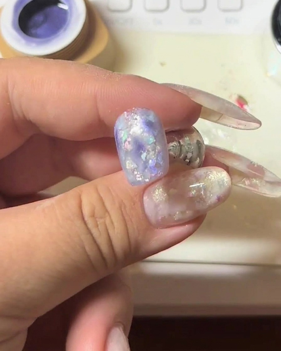 A close-up of a nail with purple cat-eye gel being held under a magnet to intensify the shimmering light strip.