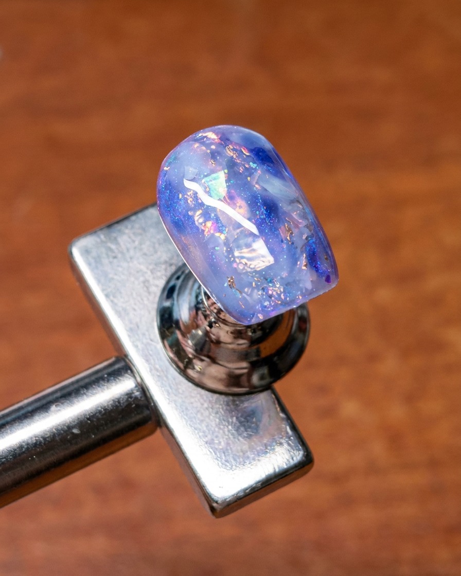 A brush being used to blend base gel over the edges of embedded shell and glitter nail art for a soft, diffused look.